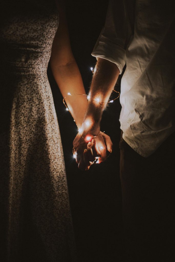 pexels-photo-792777-792777 A warm and intimate close-up of a couple holding hands adorned with glowing string lights.